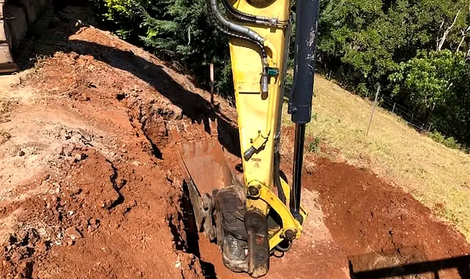 Excavator bucket digging a red-soil trench